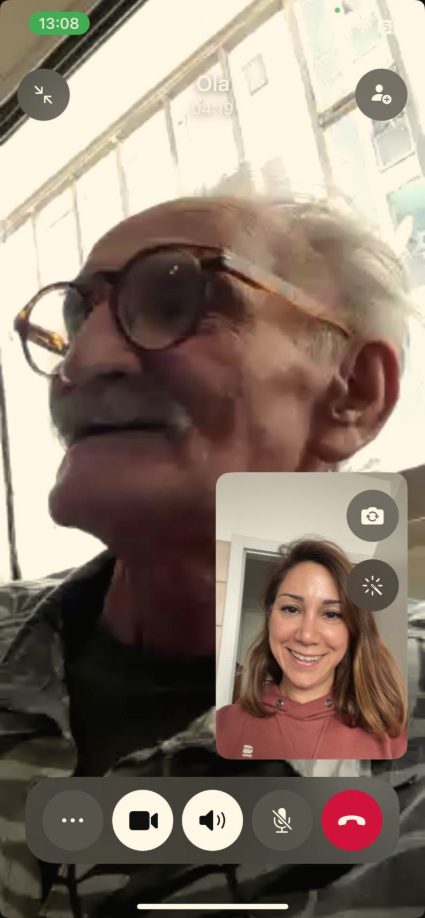 Video call: Dela's father by a bright window, Dela smiling in the corner window.